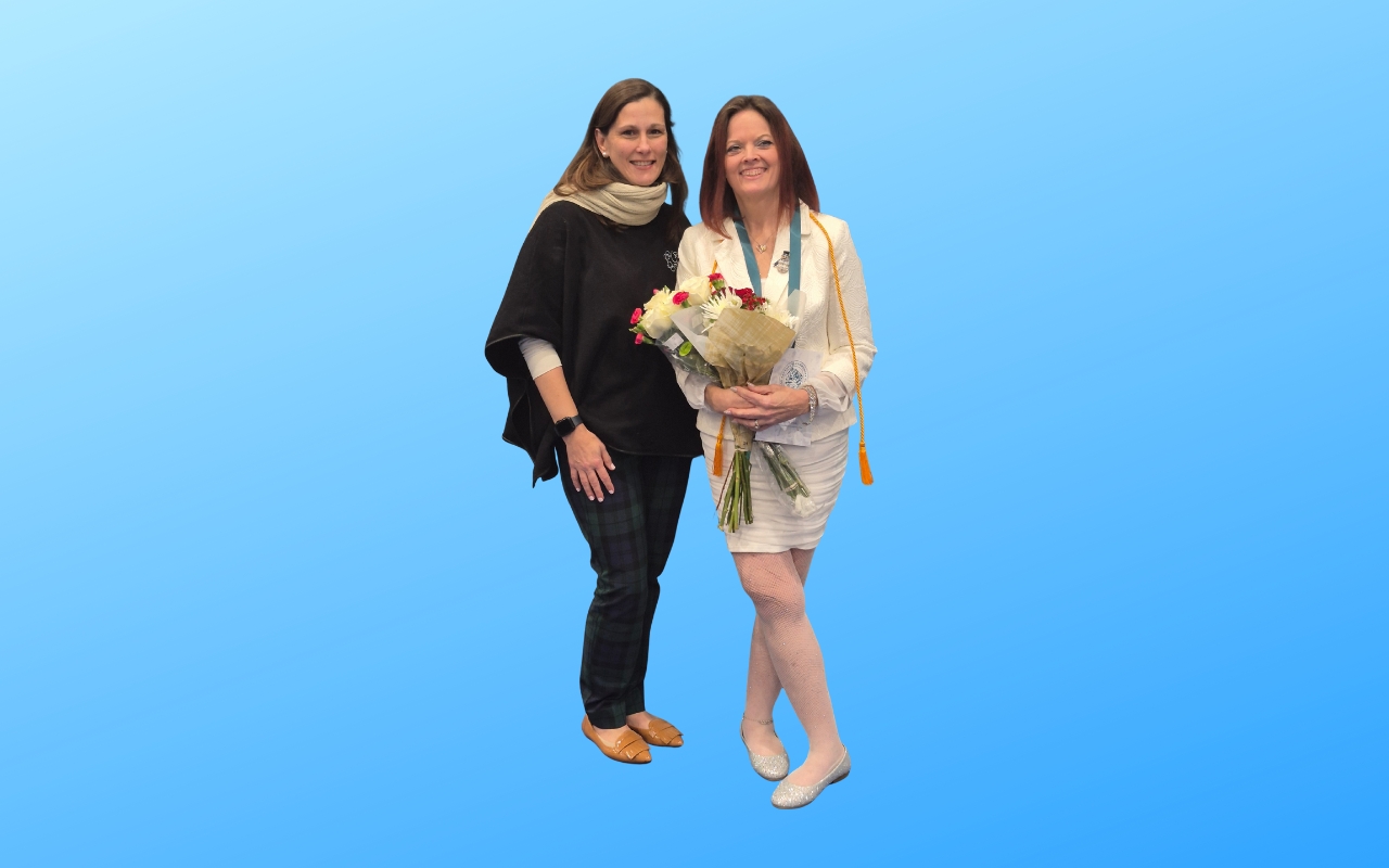 Second-career nurse Carrie Rodevick celebrates graduation, standing in a hallway holding flowers beside a family member