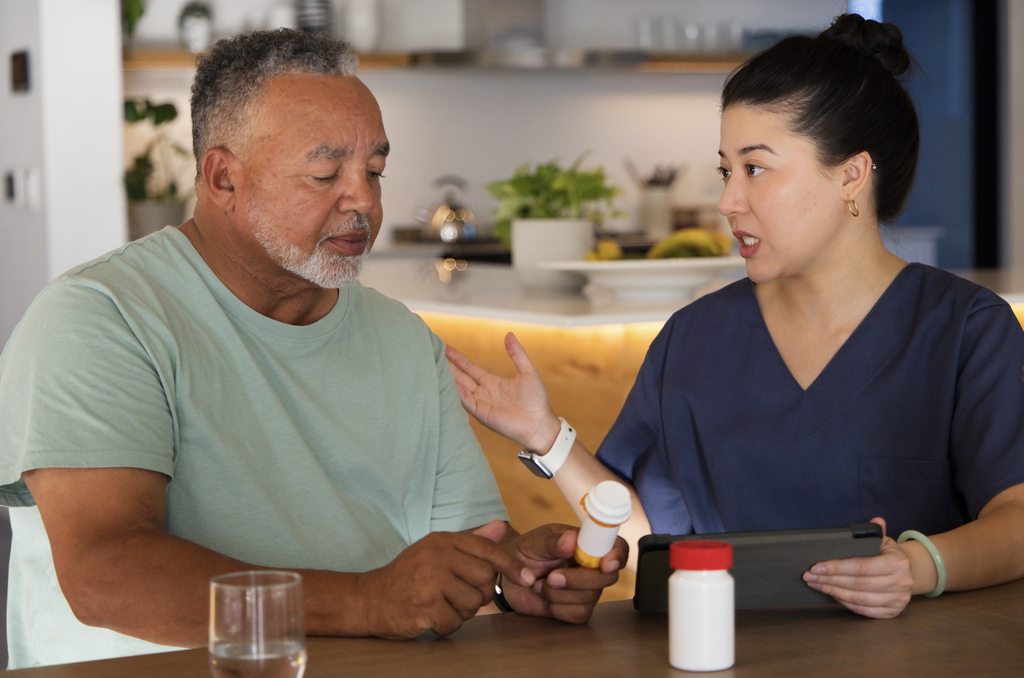 both seated at a table, a female nurse holding a tablet in her hand reviewing medications with a male patient. 